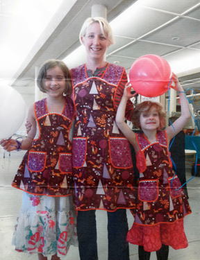 A mother with two daughters are modeling matching aprons.