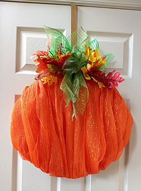 A very unusual pumpkin wreath, using pumpkin orange organdy stretched over a round form with green and brown ribbons at top for leaves and stem.