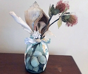 Shown is a single glass vase with stones inside, holding silk flowers.