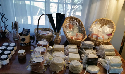 A desktop in front of a home window shows many wrapped soaps and bath salves.