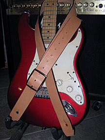 Showing a guitar with a leather guitar strap attached that has no design indented in it.