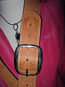 Showing a close up of a guitar strap on a guitar which has a handsome Spanish-brocade design indented in it.