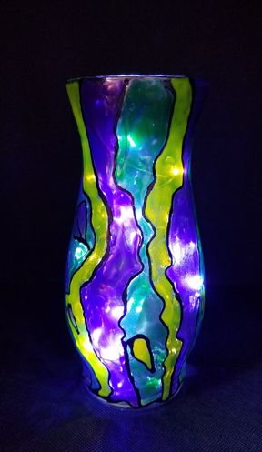 A tall narrow vase with unusual shaping has been beautifully decorated as if stained glass.