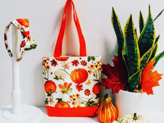 A cloth bag with a pumpkins and Fall flowers theme fabric. A head-band hangs beside it made of the same fabric.
